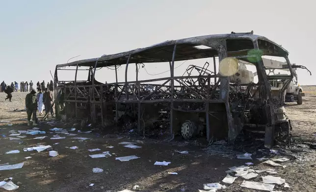People and soldiers from the Taliban army inspect a burned-out bus that collided with a truck and a motorbike Tuesday evening, causing a massive fire and killing at least 70 people, including children, most of them Afghans returning from Iran, in western Herat province, Afghanistan, Wednesday, Aug. 20, 2025. (AP Photo/Omid Haqjoo)