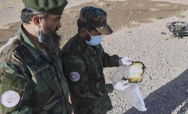A medic from the Taliban army collects items at the site where a burned-out bus collided with a truck and a motorbike Tuesday evening, causing a massive fire and killing at least 70 people, including children, most of them Afghans returning from Iran, in western Herat province, Afghanistan, Wednesday, Aug. 20, 2025. (AP Photo/Omid Haqjoo)