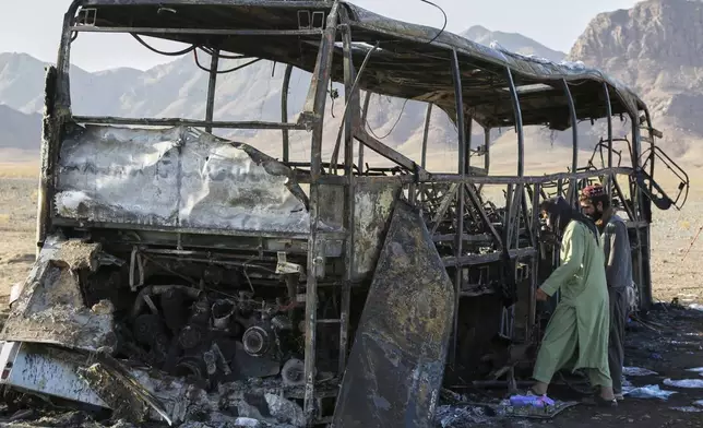 People inspect a burned-out bus that collided with a truck and a motorbike Tuesday evening, causing a massive fire and killing at least 70 people, including children, most of them Afghans returning from Iran, in western Herat province, Afghanistan, Wednesday, Aug. 20, 2025. (AP Photo/Omid Haqjoo)