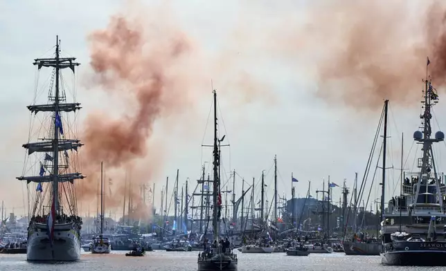 Orange smoke signals the start of the parade of hundreds of tall ships sailing into the Dutch capital's harbor for the 10th edition of SAIL, in Amsterdam, Netherlands, Wednesday, Aug. 20, 2025. (AP Photo/Peter Dejong)