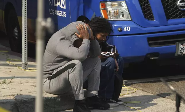 People behind police lines react as the Los Angeles Coroner van picks victims after a mass shooting during a music festival after-party in downtown Los Angeles, Monday, Aug. 4, 2025. (AP Photo/Damian Dovarganes)