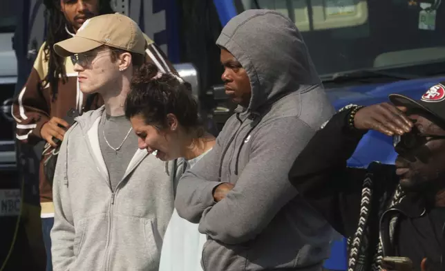 People behind police lines react as the Los Angeles Coroner van picks victims after a mass shooting during a music festival after-party in downtown Los Angeles, Monday, Aug. 4, 2025. (AP Photo/Damian Dovarganes)