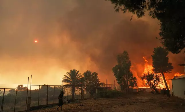 A male youth walks nearby as the fire approaches a house during a wildfire in Patras city, western Greece, Wednesday, Aug. 13, 2025. (AP Photo/Thanassis Stavrakis)