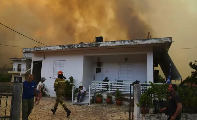 A firefighter runs at a house as a fire approaching a house during a wildfire in Vounteni, on the outskirts of Patras, western Greece, Wednesday, Aug. 13, 2025. (AP Photo/Thanassis Stavrakis)