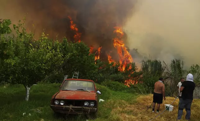 Men watch a wildfire in Vounteni, in the outskirts of Patras, western Greece, Wednesday, Aug. 13, 2025. (AP Photo/Thanassis Stavrakis)