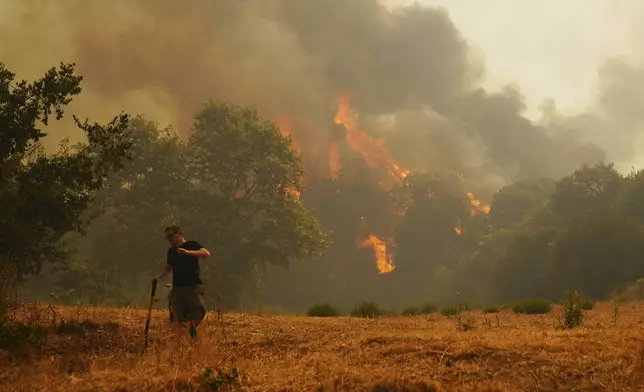 A man fights against a wildfire in Vounteni village, on the outskirts of Patras, western Greece, Wednesday, Aug. 13, 2025. (AP Photo/Thanassis Stavrakis)
