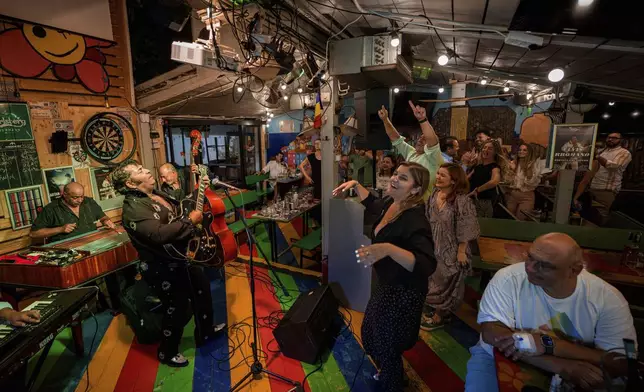 Customers dance as Tudor Lakatos, who goes by the stage name Elvis Rromano, performs at the Terasa Florilor restaurant with the Taraful Frunzelor band, in Bucharest, Romania, Friday, June 20, 2025. (AP Photo/Andreea Alexandru)
