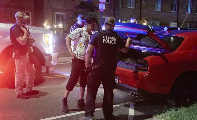 Agents from various agencies including Bureau of Alcohol, Tobacco, Firearms and Explosives, Park Police, and FBI, question a couple who had been parked outside a legal parking zone while eating McDonald's takeout, Tuesday, Aug. 12, 2025, in northwest Washington near Kennedy St. NW. The couple were released after a search of the car. (AP Photo/Jacquelyn Martin)