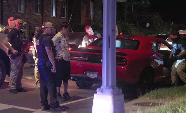 Agents from various agencies including Bureau of Alcohol, Tobacco, Firearms and Explosives, Park Police, and FBI, question a couple who had been parked in a car with Washington D.C. plates outside of a legal parking spot while eating McDonald's takeout, Tuesday, Aug. 12, 2025, in northwest Washington near Kennedy St. NW. The couple were released after a search of the car. (AP Photo/Jacquelyn Martin)