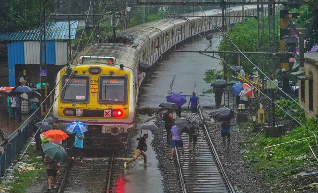 Commuters walk on waterlogged railway tracks after trains were disrupted due to heavy rainfall in Mumbai, India, Tuesday, Aug. 19, 2025. (AP Photo/ Rafiq Maqbool)