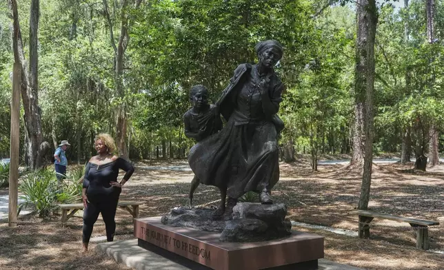 A visitor poses for a photo next to a statue of Harriet Tubman and a child titled "Journey to Freedom," at Historic Mitchelville Freedom Park on Hilton Head Island, Sunday, July 20, 2025. (AP Photo/Luis Andres Henao)