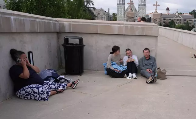 CORECTS TO PEOPLE, NOT POLICE - People shelter behind a wall on the Villanova University campus in Villanova, Pa., on Thursday, Aug. 21, 2025, where an active shooter was reported. (AP Photo/Matt Slocum)