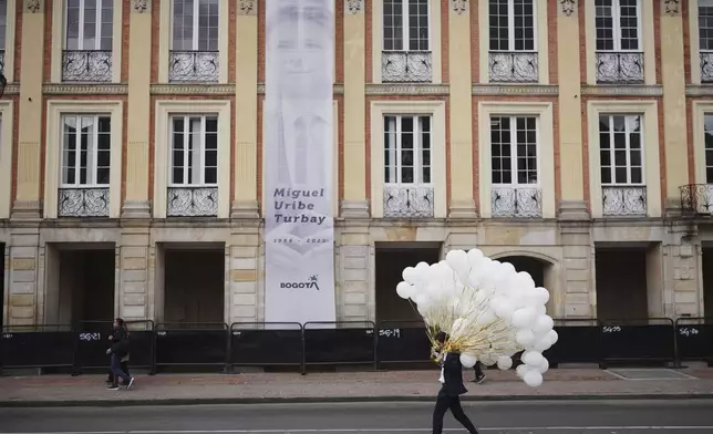 A man carries balloons past a banner honoring presidential hopeful and opposition Sen. Miguel Uribe, who died of gunshot wounds sustained at a political rally, before his funeral Mass in Bogota, Colombia, Wednesday, Aug. 13, 2025. (AP Photo/Ivan Valencia)