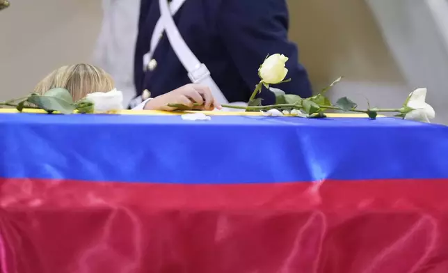 Alejandro Uribe places a flower on the coffin of his father, presidential hopeful and opposition Sen. Miguel Uribe, during his memorial service at the cathedral in Bogota, Colombia, Wednesday, Aug. 13, 2025. Uribe died from wounds suffered when he was shot at a political rally. (AP Photo/Fernando Vergara)