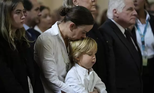CORRECTS SPELLING OF TARAZONA'S MIDDLE NAME - Maria Claudia Tarazona kisses her son Alejandro during the funeral service for her husband, presidential hopeful and opposition Sen. Miguel Uribe, who died from wounds suffered when he was shot at a political rally, in Bogota, Colombia, Wednesday, Aug. 13, 2025. At right is Miguel Uribe, the senator's father. (AP Photo/Fernando Vergara)