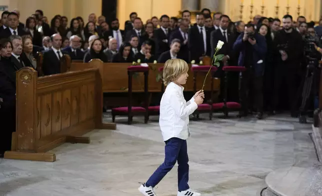 Alejandro Uribe brings a flower to the coffin of his father, presidential hopeful and opposition Sen. Miguel Uribe, who died from wounds suffered when he was shot at a political rally, during his memorial service at the cathedral in Bogota, Colombia, Wednesday, Aug. 13, 2025. (AP Photo/Fernando Vergara)