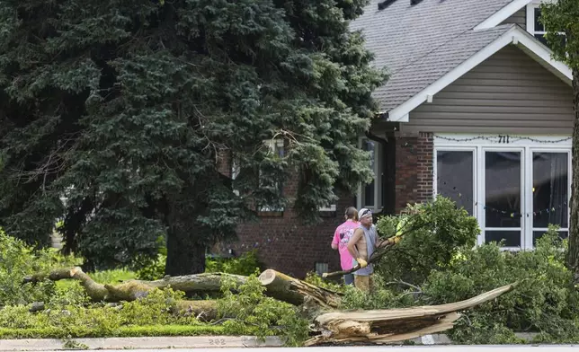 People cleen up tree debris near Lincoln and 14th Streets in Fort Calhoun, Neb. on Saturday, Aug. 9, 2025, after an early morning storm caused widespread wind damage in the area. (Chris Machian/Omaha World-Herald via AP)