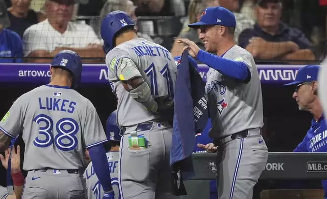 Toronto Blue Jays' Myles Straw, right, puts on a jacket for Bo Bichette as he returns to the dugout after hitting a three-run home run off Colorado Rockies relief pitcher Carson Palmquist in the seventh inning of a baseball game Monday, Aug. 4, 2025, in Denver. (AP Photo/David Zalubowski)