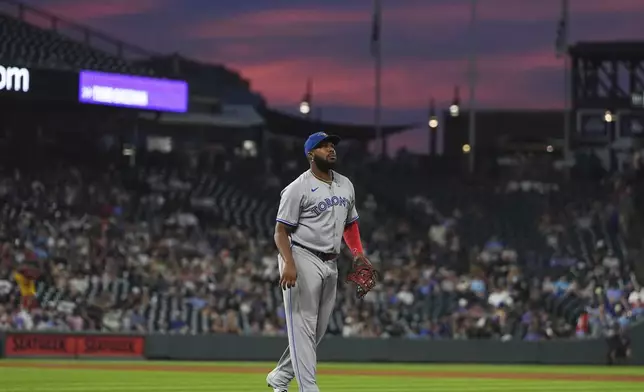 As the setting sun colors the sky above Coors Field, Toronto Blue Jays first baseman Vladimir Guerrero Jr. heads back to his position in the fifth inning of a baseball game against the Colorado Rockies, Monday, Aug. 4, 2025, in Denver. (AP Photo/David Zalubowski)