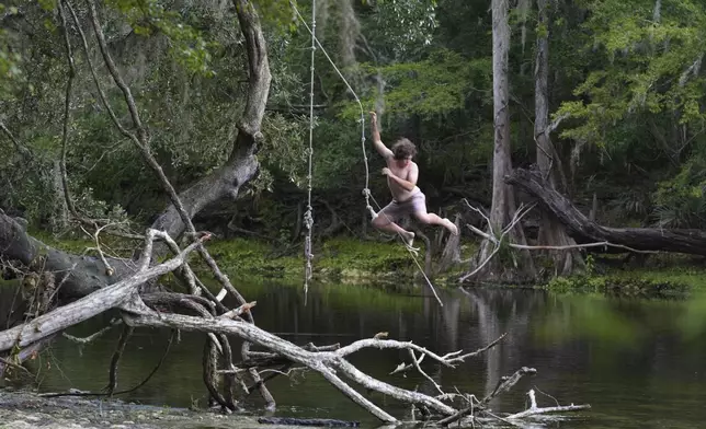 Gage Williams swings from a branch near the confluence of Poe Spring and the Santa Fe River on Tuesday, July 15, 2025, in Alachua County, Fla. (AP Photo/Marta Lavandier)