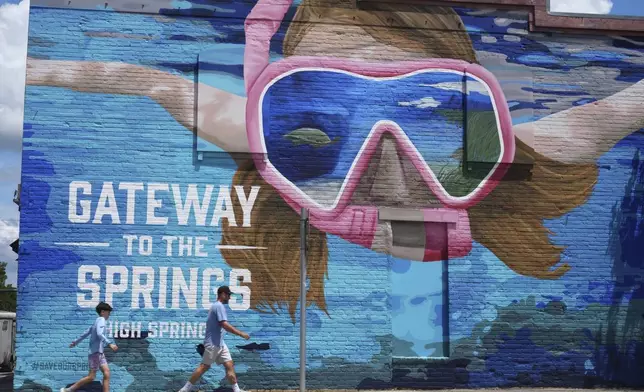 A father and son walk along a mural Wednesday, July 16, 2025, in High Springs, Fla. (AP Photo/Marta Lavandier)