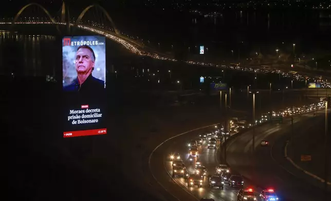 FILE - An electronic billboard with an image of President Jair Bolsonaro and text that reads in Portuguese: "Moraes orders house arrest for Bolsonaro," towers over a caravan of supporters protesting the house arrest order, in Brasilia, Brazil, Aug. 4, 2025. (AP Photo/Luis Nova, File)