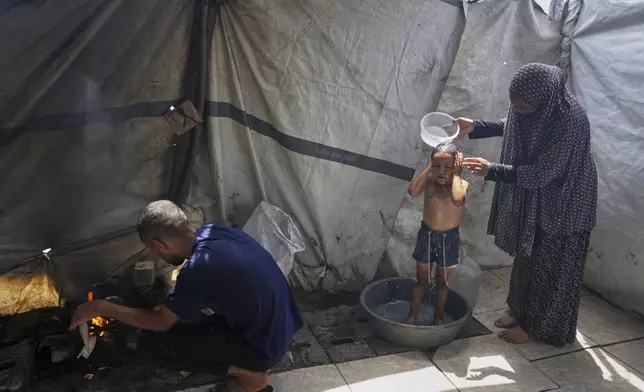 Enaam Al Majdoub uses water collected from a distribution point to bathe her 3-year-old granddaughter, Jourieh, while her son Zaki uses some of the water for cooking in their family tent in Gaza City on Tuesday, August 12, 2025. (AP Photo/Jehad Alshrafi)