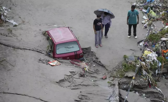 People stand next to a stuck car in the aftermath of flash floods at the banks of Tawi river in Jammu, India, Wednesday, Aug. 27, 2025. (AP Photo/Channi Anand)
