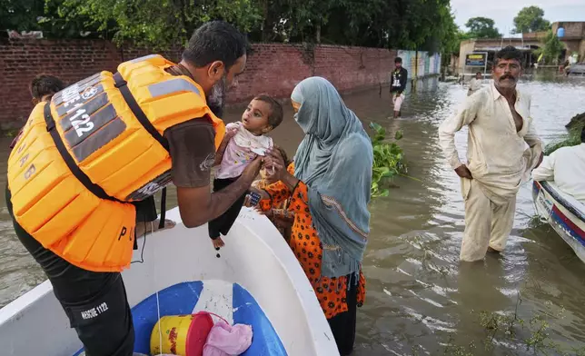 A rescue worker helps a family board in a boat to evacuate them from a flooded area in Dhoop Sarhi village in Kasur district, Pakistan, Tuesday, Aug. 26, 2025, due to the rising water level in Sutlej River, following neighboring India releasing water from overflowing dams. (AP Photo/K.M. Chaudary)