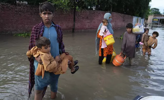A family walk toward a rescue boat arriving to evacuate them from a flooded area in Dhoop Sarhi village in Kasur district, Pakistan, Tuesday, Aug. 26, 2025, due to the rising water level in Sutlej River, following neighboring India releasing water from overflowing dams. (AP Photo/K.M. Chaudary)