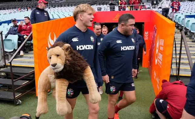 Henry Pollock of the British &amp; Irish Lions, left, carries his team's mascot as he arrives for their captain's run training session in Sydney, Australia, Friday, Aug. 1, 2025, ahead of their rugby union test match against Australia on Saturday. (AP Photo/Rick Rycroft)
