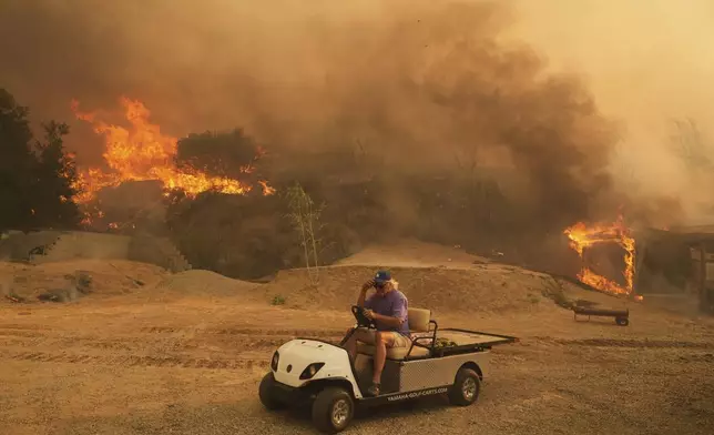 A resident rides a golf cart as he exits his property while the Canyon Fire burns on Thursday, Aug. 7, 2025, in Halsey Canyon, Calif. (AP Photo/Marcio Jose Sanchez)
