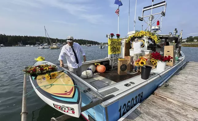 Lobsterman Josh Hupper adds flowers to Sunshine Stewart's paddleboard prior to a memorial service, Sunday, Aug. 10, 2025, in St. George, Maine. (AP Photo/Robert F. Bukaty)