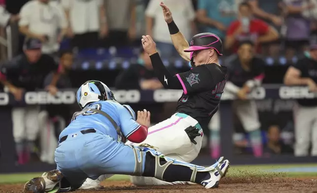 Miami Marlins' Troy Johnston, left, gets tagged out by Toronto Blue Jays catcher Alejandro Kirk (30) during the seventh inning of a baseball game, Saturday, Aug. 23, 2025, in Miami. (AP Photo/Jim Rassol)