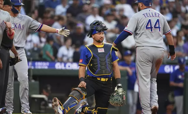 Seattle Mariners catcher Cal Raleigh looks on as Texas Rangers' Rowdy Tellez (44) greets teammate Corey Seager after scoring on a single by Josh Smith during the third inning of a baseball game Friday, Aug. 1, 2025, in Seattle. (AP Photo/Lindsey Wasson)