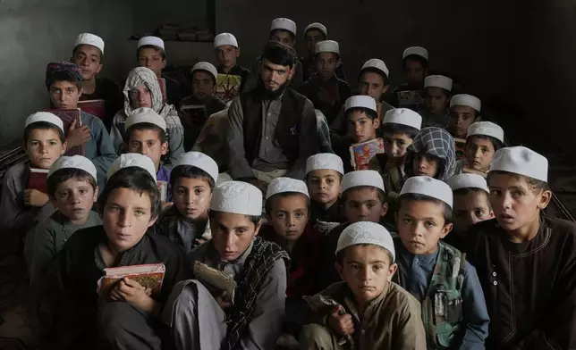 Afghan boys pose for a photo with their teacher during a Quran class at the Abdullah Ibn-Masoud religious school in the outskirts of Kabul, Afghanistan, Monday, May 26, 2025. (AP Photo/Ebrahim Noroozi)