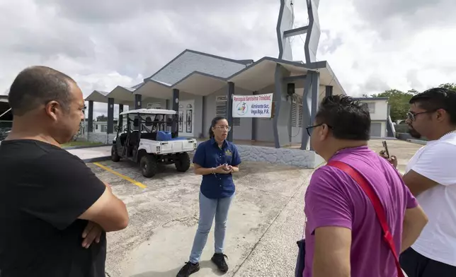 A tour guide talks to visitors outside Parroquia Santísima Trinidad, where Bad Bunny served as an altar boy, in Vega Baja, Puerto Rico, Tuesday, Aug. 12, 2025. (AP Photo/Alejandro Granadillo)