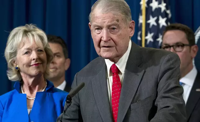 FILE - Former FBI director and CIA director William Webster, right, accompanied by his wife Lynda Webster, who were targeted by a man who peddled a lottery scam over phone calls and emails, speaks during a news conference to address elder financial exploitation and law enforcement actions, at the Department of Justice in Washington, March 7, 2019. (AP Photo/Jose Luis Magana, File)