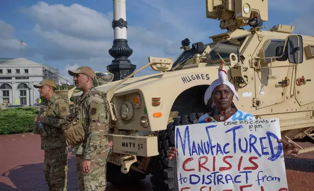 Protester Nadine Seiler holds her sign near National Guard members from the 167th Security Forces from West Virginia, outside Union Station in Washington, Wednesday, Aug. 20, 2025. (AP Photo/Rod Lamkey, Jr.)