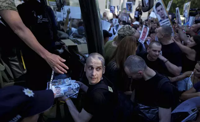 Ukrainian soldiers walk though a crowd of people holding photos of their missing relatives after returning from captivity after a POWs exchange between Russia and Ukraine, in Chernyhiv region, Ukraine, Thursday, Aug. 14, 2025. (AP Photo/Evgeniy Maloletka)
