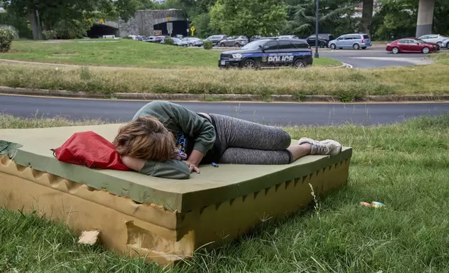 Stephanie W., 28, who is homeless, rests on a foam mattress as a United States Park Police vehicle drives past, Wednesday, Aug. 13, 2025, in northwest Washington near the Kennedy Center. (AP Photo/Jacquelyn Martin)