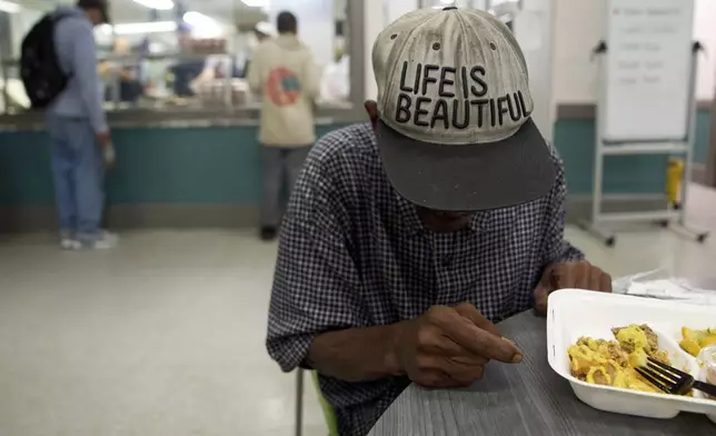 A guest of Miriam's Kitchen wears a hat saying, "Life is Beautiful," as he eats a meal, Wednesday, Aug. 13, 2025, at the organization which serves food to people who are homeless, in Washington. (AP Photo/Jacquelyn Martin)