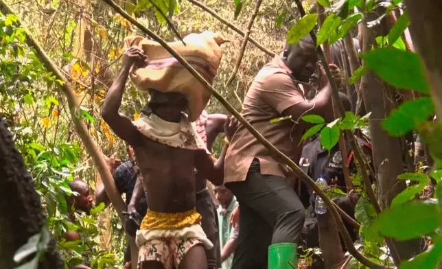 In this image taken from video, a man carries bodies retrieved from the military helicopter crash in Sikaman near Adansi, Ashanti region, Ghana, Wednesday, Aug. 6, 2025. (AP Photo/Hafiz Tijani)