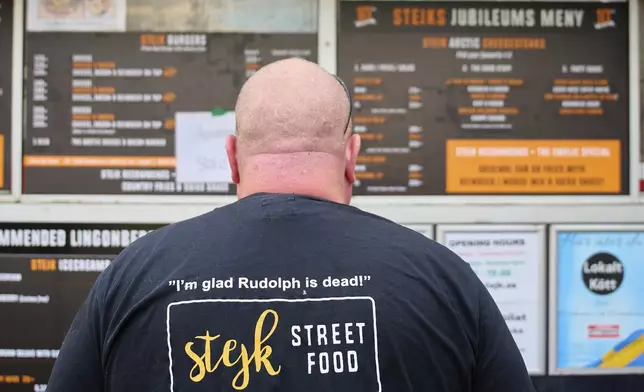 Zebastian Bohman, a co-owner of Stejk Street Food, wears a t-shirt that reads "I'm glad Rudolph is dead", standing outside his food truck in Kiruna, Sweden, Sunday, Aug. 17, 2025. (AP Photo/Malin Haarala)