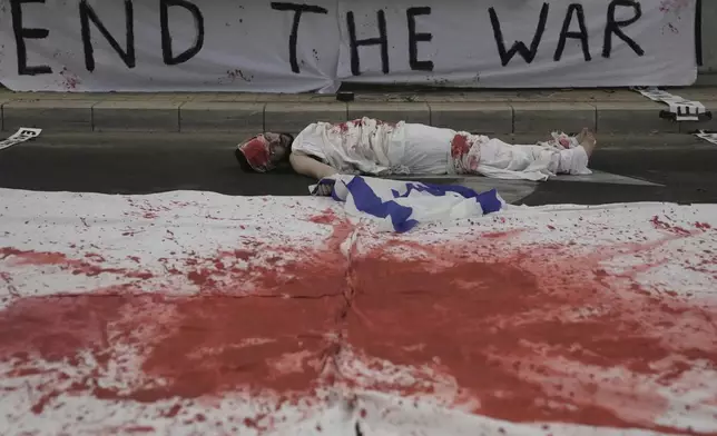 A demonstrator lies on the ground painted in red, symbolizing blood, during a protest demanding the end of the war, the immediate release of hostages held by Hamas in the Gaza Strip, and against Prime Minister Benjamin Netanyahu's government in Tel Aviv, Israel, Saturday, Aug. 16, 2025. (AP Photo/Mahmoud Illean)