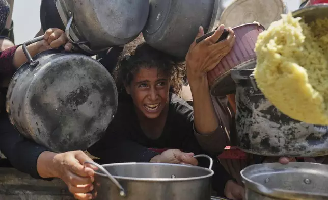 A Palestinian girl struggles to get donated food at a community kitchen in Gaza City, northern Gaza Strip, Saturday, Aug. 16, 2025. (AP Photo/Jehad Alshrafi)