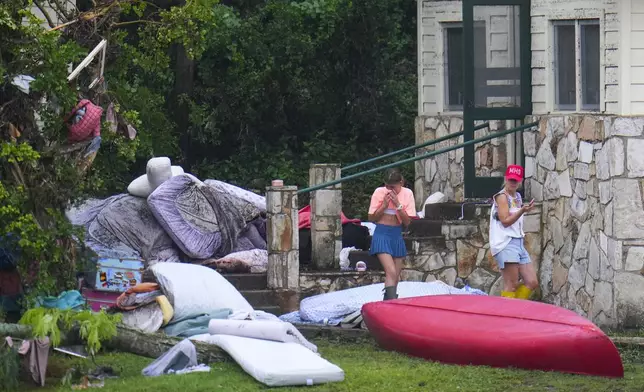People walk amid the belongings of campers outside the sleeping area of Camp Mystic along the banks of the Guadalupe River, July 6, 2025, in Hunt, Texas, after a deadly flash flood swept through the area on Independence Day. (AP Photo/Julio Cortez)