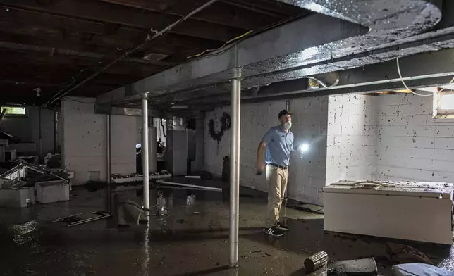 A structural engineer surveys a friend's home with flooding, Monday, Aug. 11, 2025, in Wauwatosa, Wis. (AP Photo/Andy Manis)