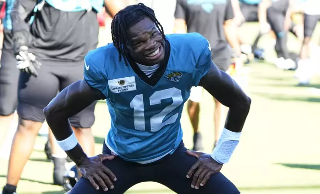 Jacksonville Jaguars wide receiver Travis Hunter (12) smiles at photographers as he warms up during practice at the team's NFL football training camp, Monday, July 28, 2025, in Jacksonville, Fla. (AP Photo/John Raoux)