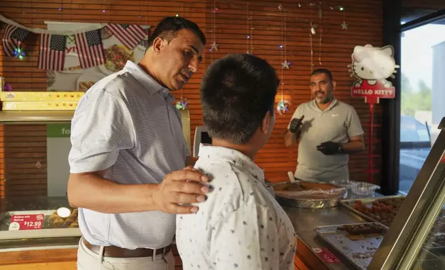 Faroz Waziri, left, helps his son decide on a piece of baklava from a halal grocery store owned by Mohamed Mahmoud, right, in Cedar Rapids, Iowa, on Friday, Aug. 8, 2025. (AP Photo/Jessie Wardarski)